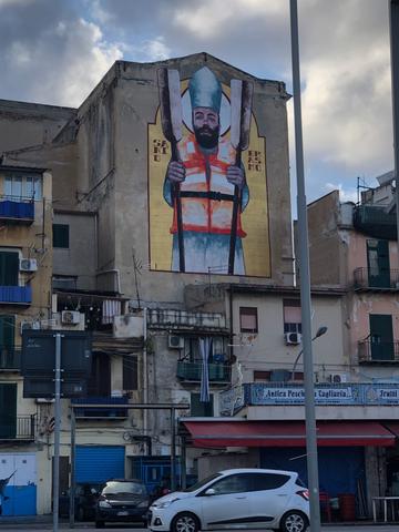 Grafiti on a blind wall of a building block featuring Sant'Erasmo holding two boat oars and wearing a life jacket.