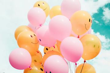low angle photo of pink and yellow ballons with sketches of facial expressions on them