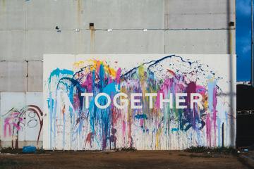 Graffiti on concrete wall. The word 'together' is written in white bold letters agains a background of colourful splash 