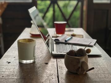 table with laptop, notepad, pen and cup of tea.
