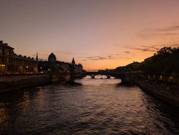 A photo of the Seine in Parin in the sunset. Both banks and a bridge are depicted.