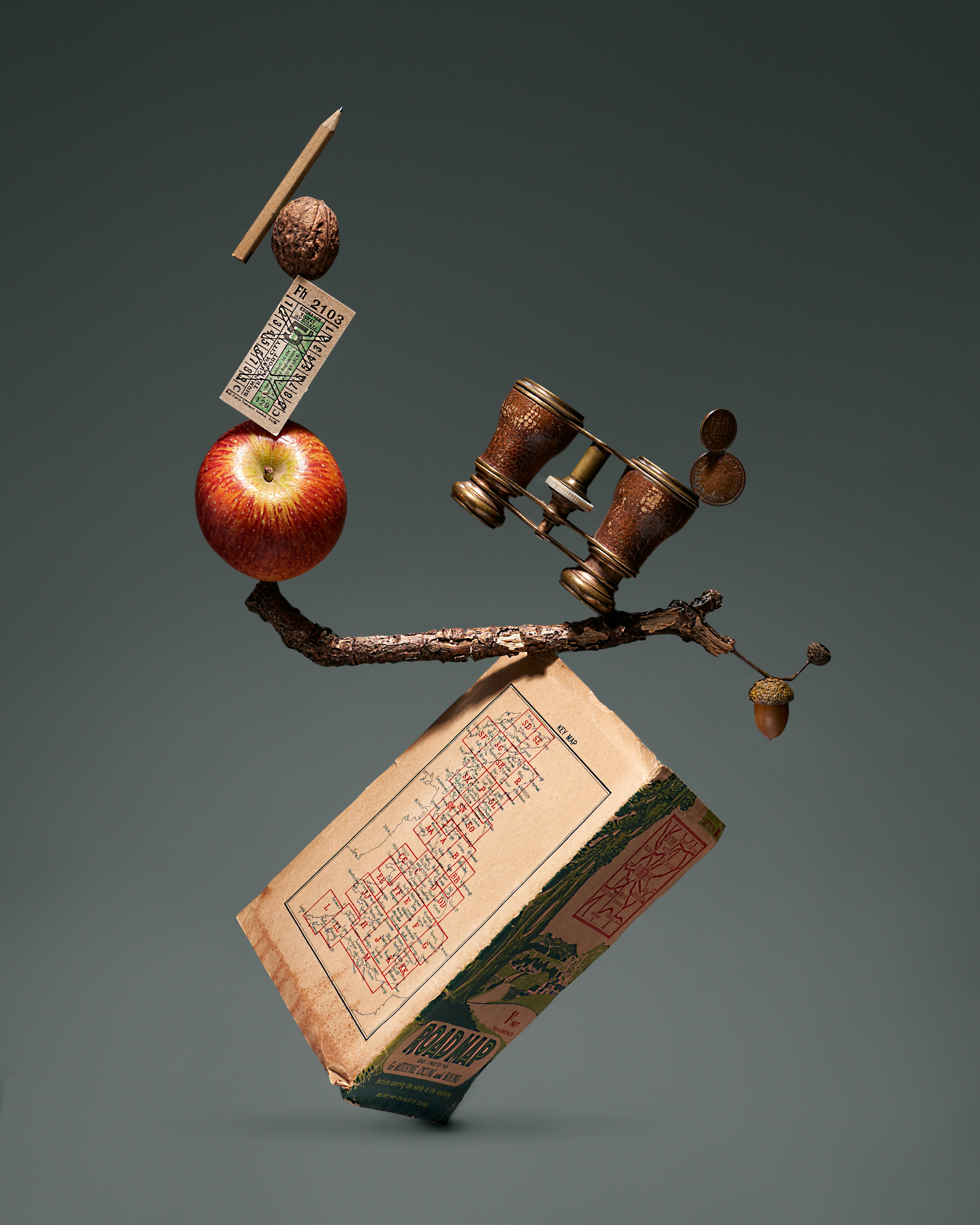 Absurd picture where a series of objects, including an apple, a pencil, a book, a pair of binoculars etc are impossibly balanced on top each other to prompt the viewer's interest.
