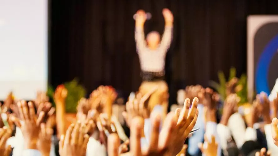 Hands of a crowd raised at a speaker on the stage