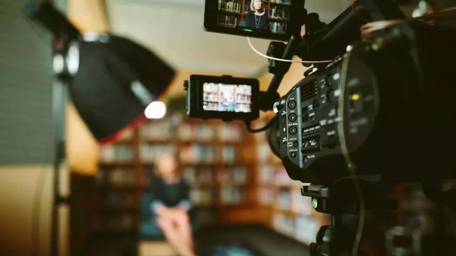 Person sitting in front of a bookshelf being filmed