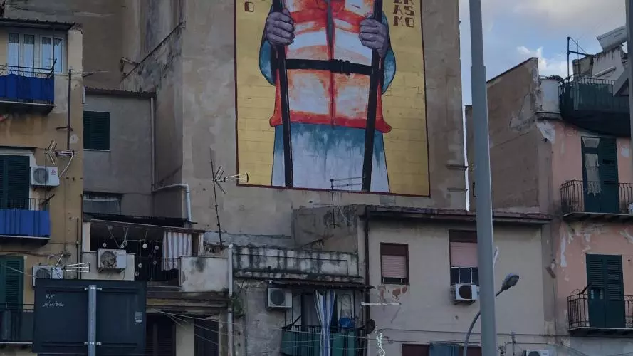 Grafiti on a blind wall of a building block featuring Sant'Erasmo holding two boat oars and wearing a life jacket.