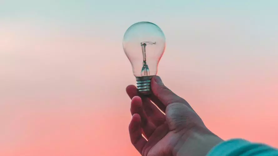 Photo of a hand holding a lightbulb against the sunset