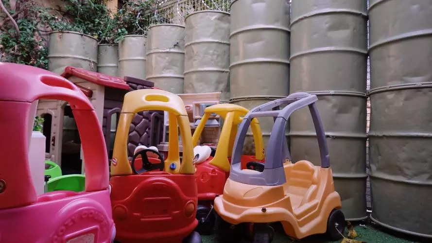 Photo of childrens' ride on toys in front of a barrier made of military barrels.