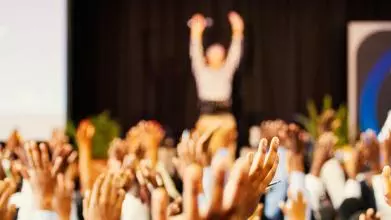 Hands of a crowd raised at a speaker on the stage