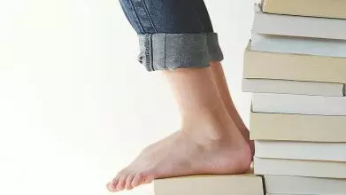 Picture of the lower body of a young person sitting on a stack of books while reading