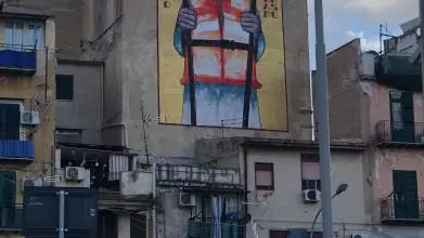 Grafiti on a blind wall of a building block featuring Sant'Erasmo holding two boat oars and wearing a life jacket.