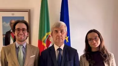 The student with two colleagues of hers in front of the Portuguese and European flags