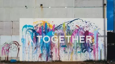 Graffiti on concrete wall. The word 'together' is written in white bold letters agains a background of colourful splash 