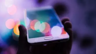 hand holding smartphone with colourful light reflections all over