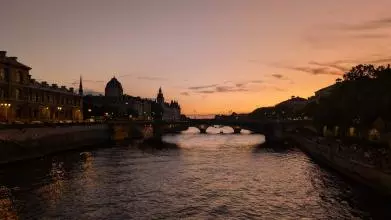 A photo of the Seine in Parin in the sunset. Both banks and a bridge are depicted.