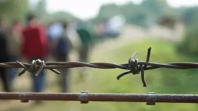 Barbed wire with blurred shapes of migrants