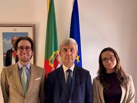 The student with two colleagues of hers in front of the Portuguese and European flags