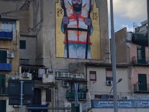 Grafiti on a blind wall of a building block featuring Sant'Erasmo holding two boat oars and wearing a life jacket.