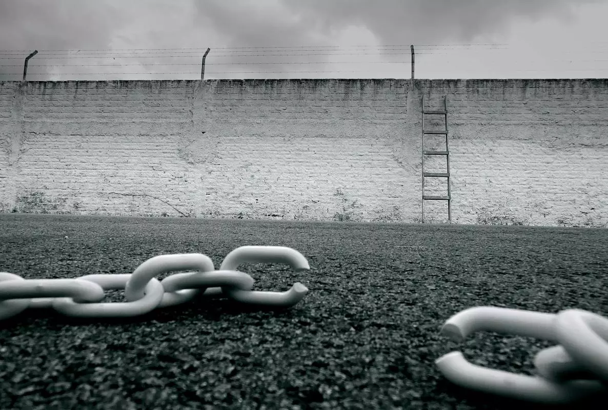 White broke chain in front of an enclosure wall. A ladder stands again the wall. 