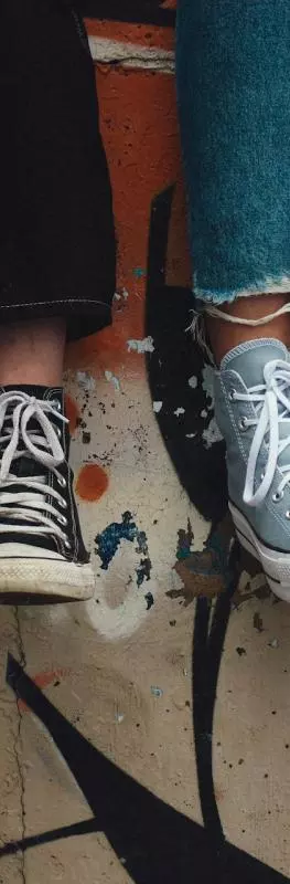 Shot of two sets of legs below the knee of two teenagers sitting on a wall with graffiti