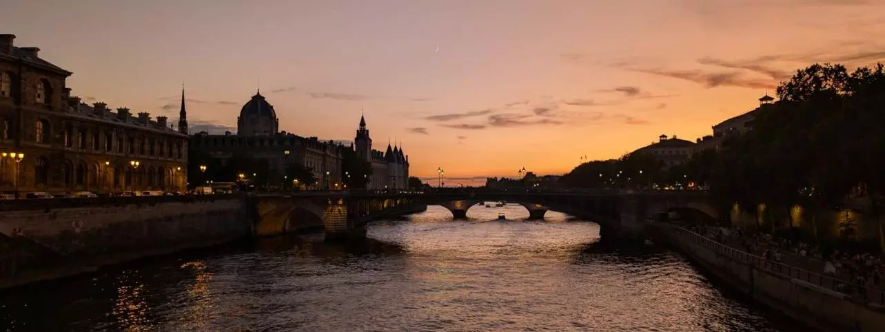 A photo of the Seine in Parin in the sunset. Both banks and a bridge are depicted.